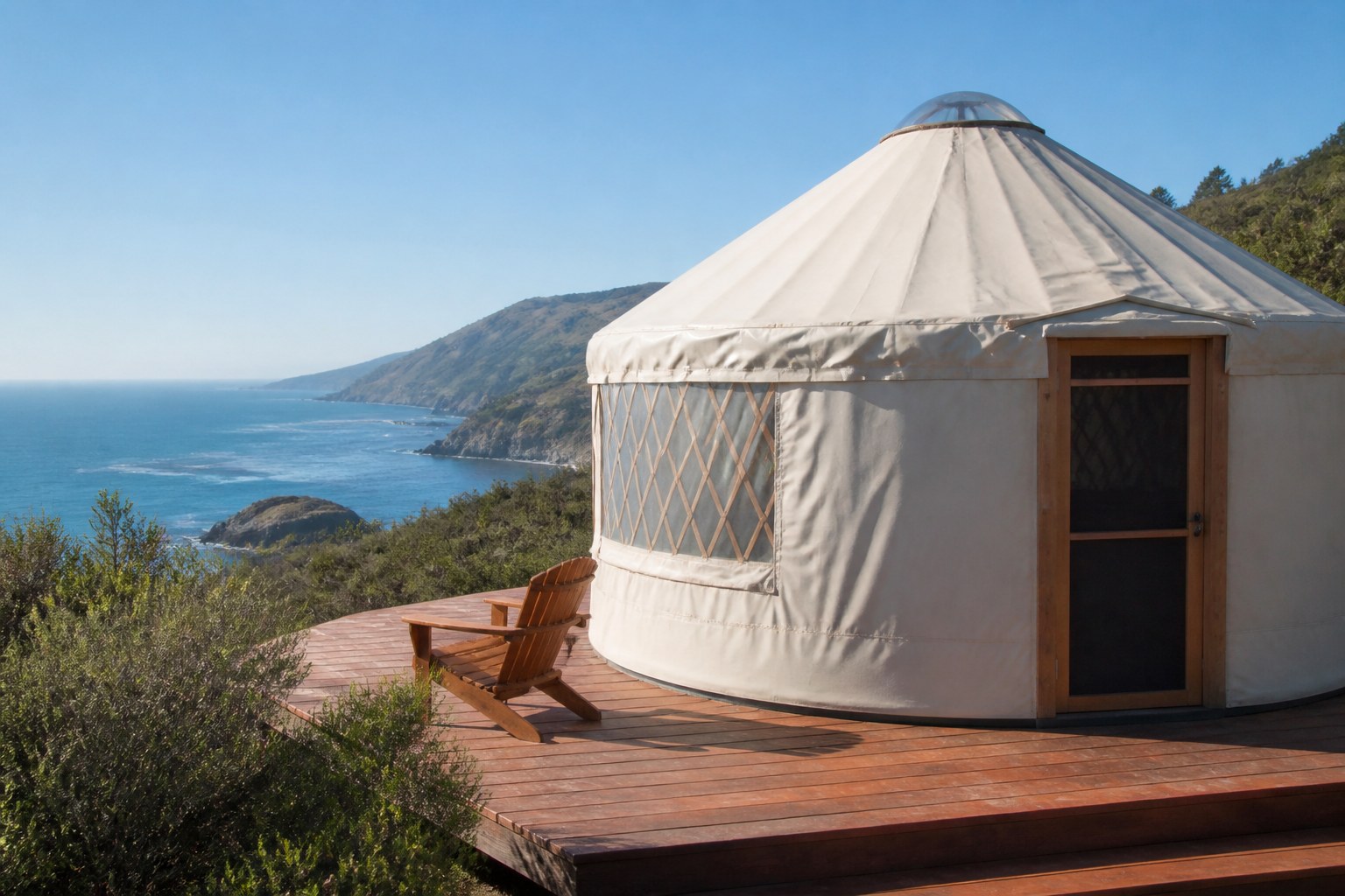 Circular white yurt with transparent skylight dome on a wooden deck overlooking the Big Sur coastline and Pacific Ocean